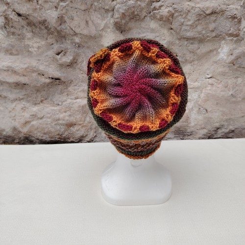 Bonnet femme tricoté à la main dans un fil multicolore chaud doux et très agréable. Le bonnet est composé de plusieurs motifs de points en jouant avec les couleurs. Le lien est tricoté avec le même fil mais dans une seule teinte. La fleur est crochetée dans ce même fil également avec une seule teinte et cousu à la main.